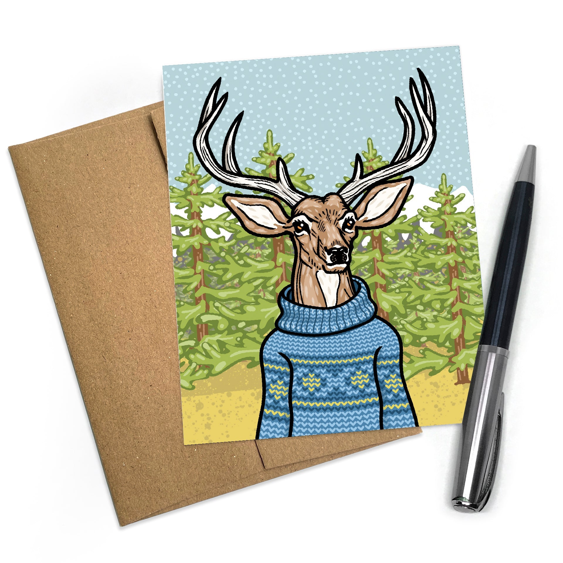 A cheerful funny sweater card featuring a deer wearing a blue sweater, surrounded by green trees and snowflakes. The card is displayed next to a brown envelope and a pen, showcasing its playful design.
