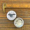 Crow button pin displayed on a wooden surface next to a ruler, highlighting its size and intricate design.
