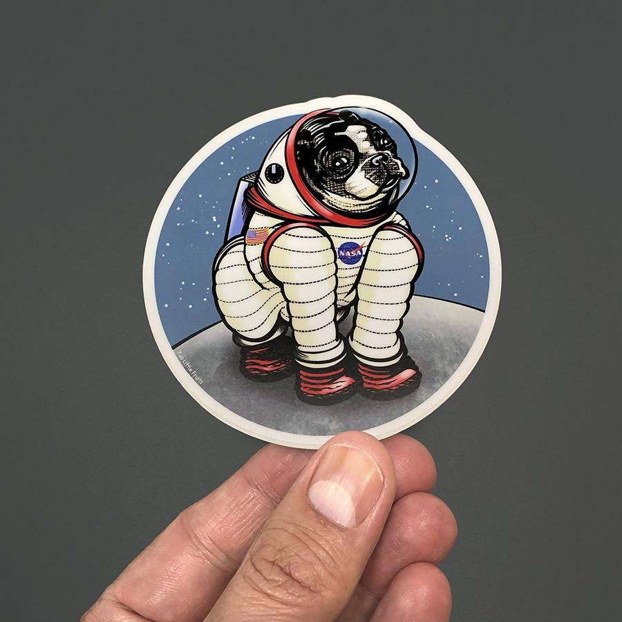 Hand holding the Rover The Space Dog Die Cut Sticker, featuring an astronaut dog against a starry background. A delightful space dog sticker for personalizing items.