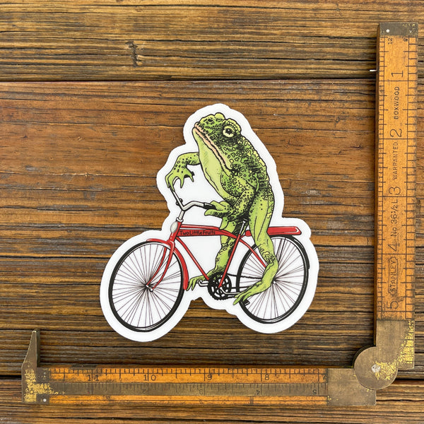 Unique frog art sticker featuring a whimsical illustration of a frog riding a vintage red bicycle, showcasing creativity and fun.