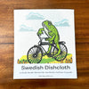 A vibrant Frog On A Bike Swedish Dishcloth lying flat, highlighting its eco-friendly materials and functionality as a compostable kitchen cloth.