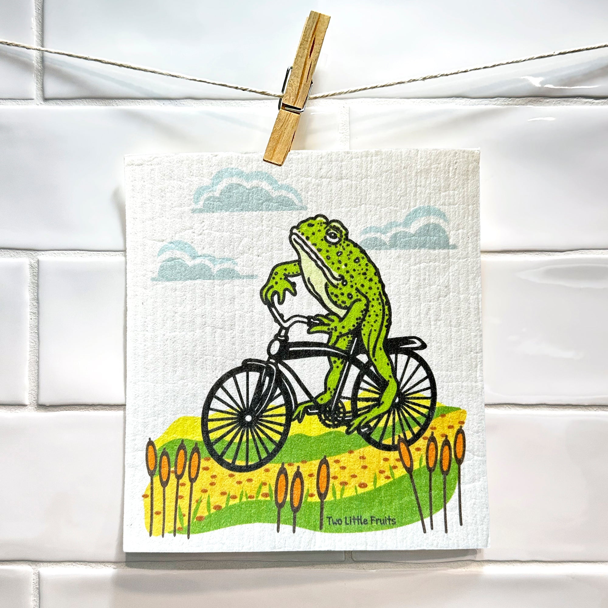 Frog On A Bike Swedish Dishcloth hung up, showcasing its fun design as a compostable kitchen cloth that brightens up your kitchen.