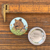 A colorful grizzly bear pin displayed next to a measuring ruler, illustrating its size of 1.25 inches, set against a rustic wooden background.