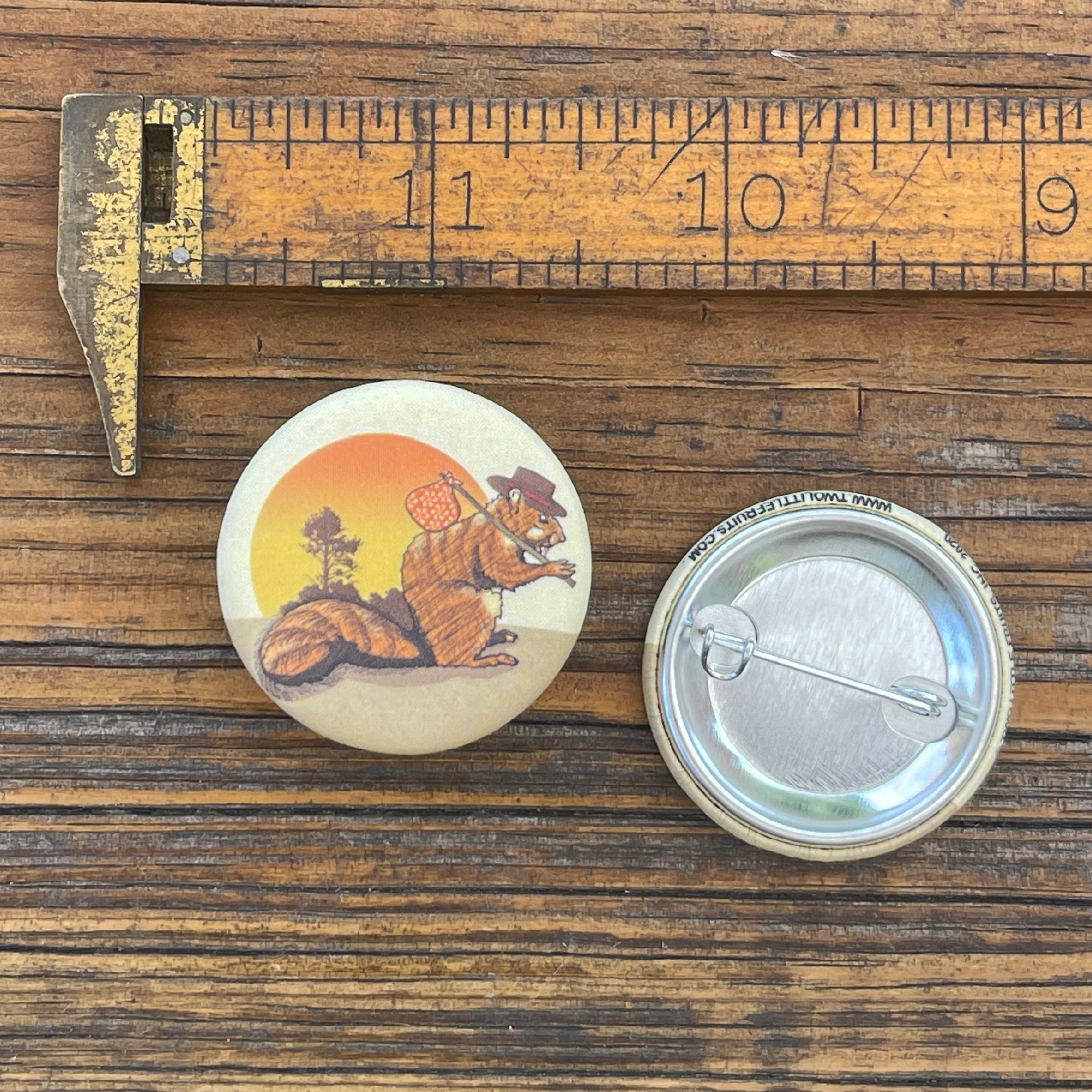 A Hobo Squirrel Button Pin featuring a whimsical illustration of a squirrel wearing a hat and carrying a bag, set against a sunset background, emphasizing Colorado pride.