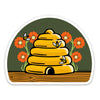 Charming beehive die cut sticker showcasing a yellow skep beehive with bees and bright flowers, ideal for adding flair to any surface.