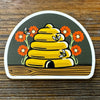 Adorable beehive die cut sticker featuring a skep beehive surrounded by colorful flowers and bees, perfect for personalizing your belongings.
