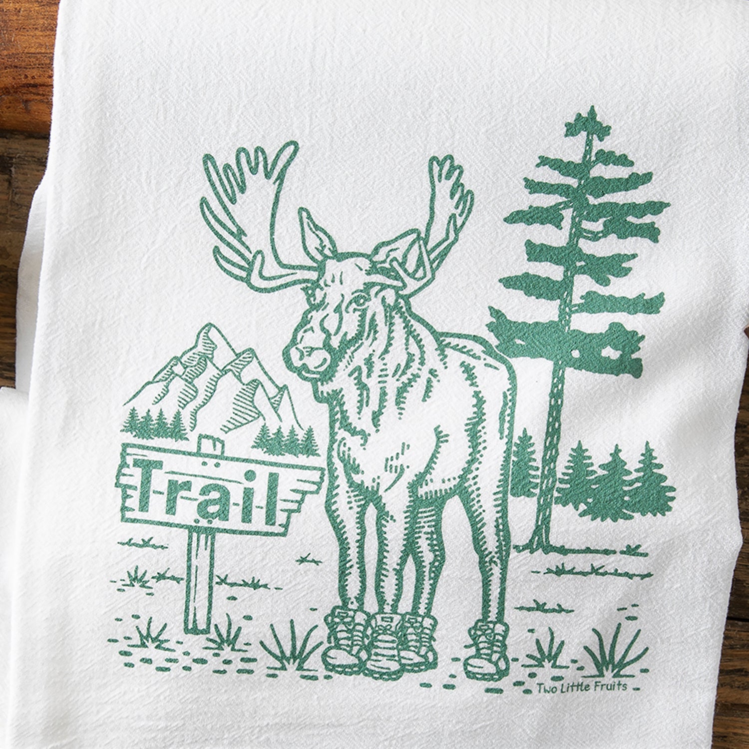Moose Kitchen Towel featuring a whimsical illustration of a moose in boots, surrounded by a pine tree and mountains, perfect for adding charm to any kitchen with cotton kitchen towels.