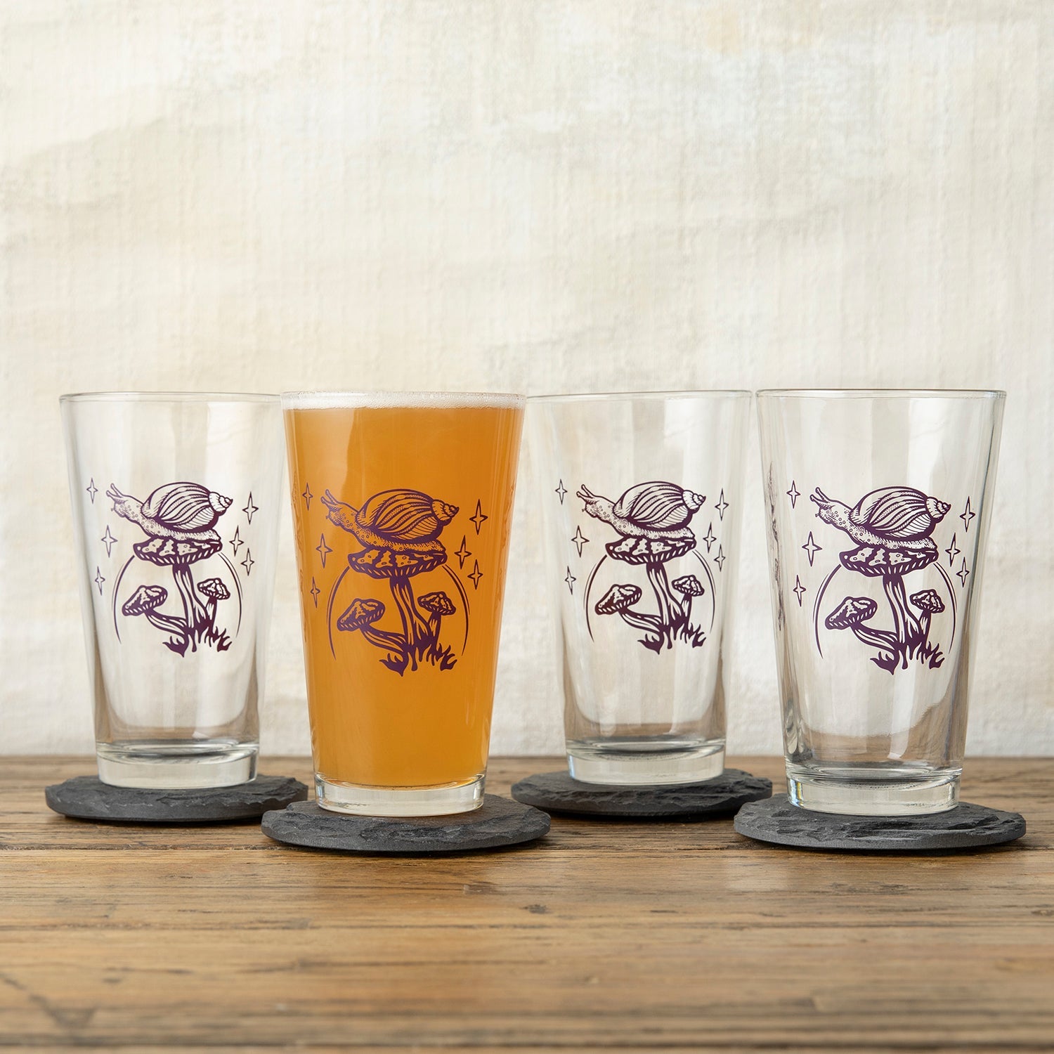 Set of four mushroom pint glasses showcasing the unique purple snail and mushroom illustration, ideal for gatherings and everyday use.