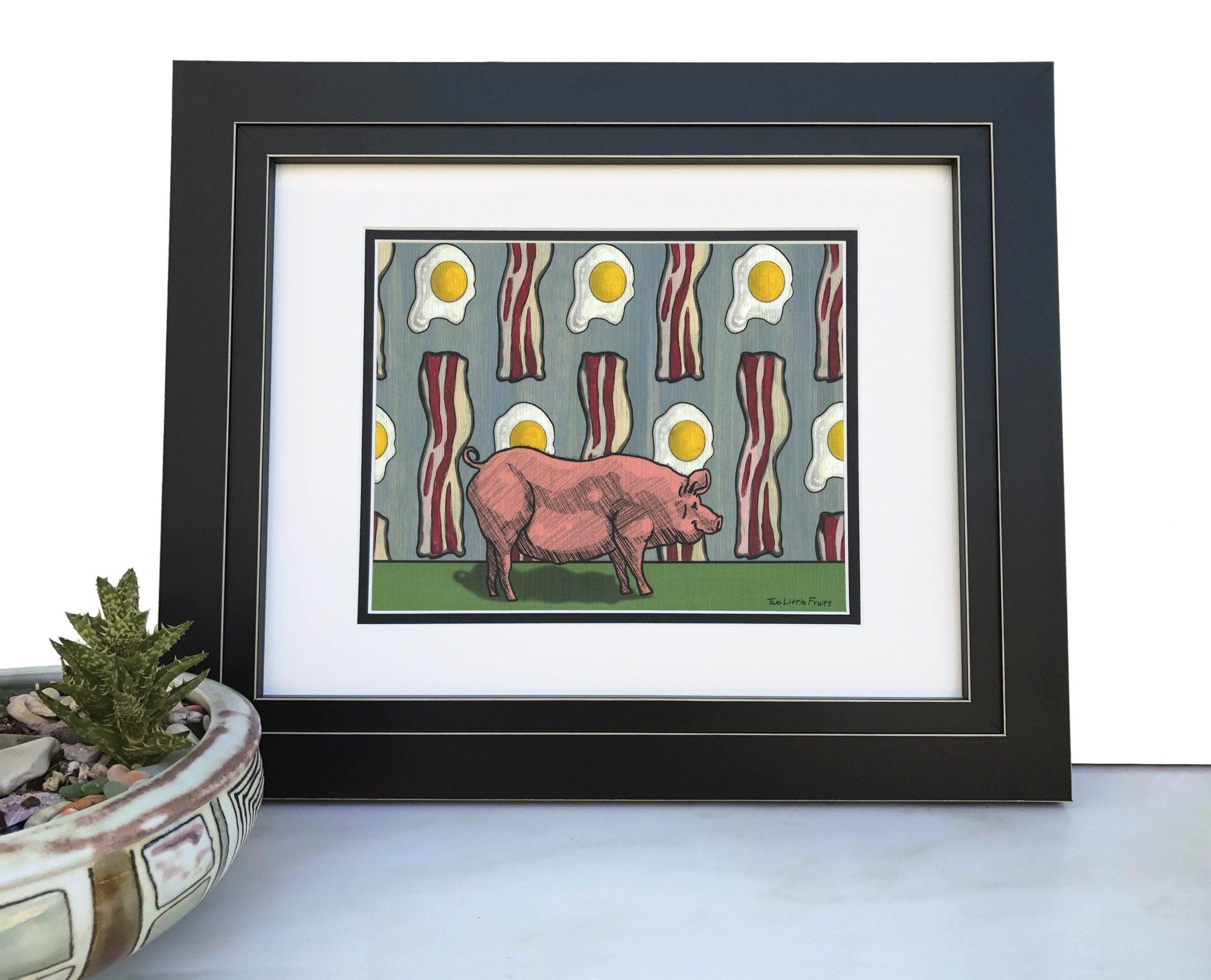 Framed Pig and Bacon Art Print featuring a pink pig standing on green grass, surrounded by a background of bacon strips and fried eggs, perfectly styled for kitchen decor.