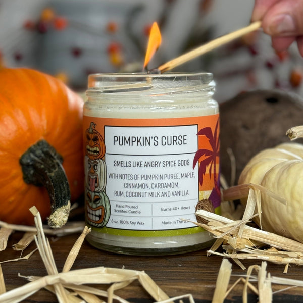 Pumpkin Spice Scented Soy Candle by Two Little Fruits, being lit with a matchstick. The label 'Pumpkin's Curse' is visible, emphasizing the rich scents of pumpkin puree, maple, and cinnamon, perfect for cozy autumn vibes with pumpkin spice candles.