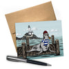 Sailor Sea Lion Blank Greeting Card with a nautical theme, featuring a sea lion wearing a striped shirt and a red beanie, sitting on a wooden dock beside a lighthouse. Perfect for sending cheerful messages.