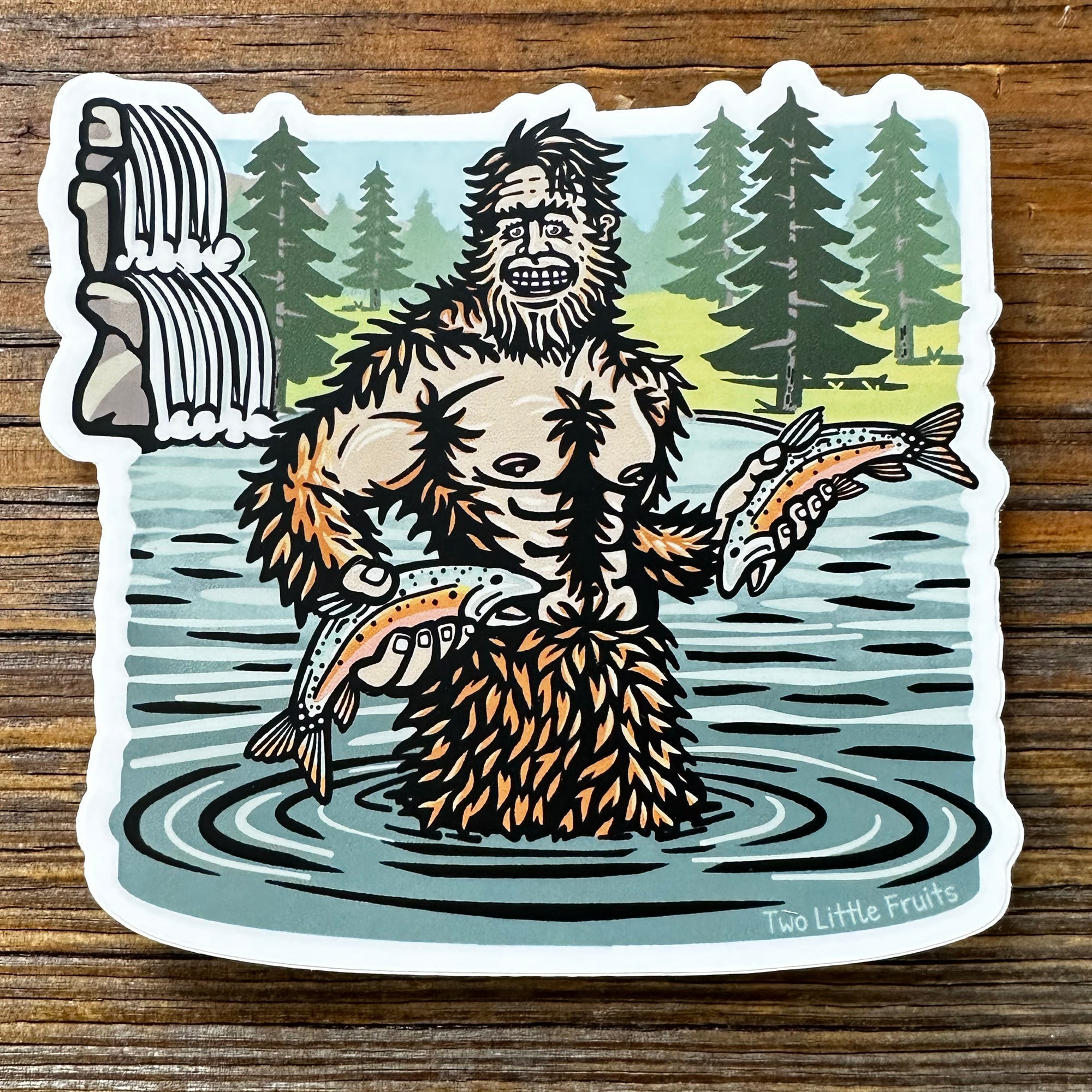 Sasquatch Sticker featuring a proud Sasquatch in the water holding fish, surrounded by trees and a waterfall, showcasing Two Little Fruits' unique illustration.