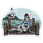 Vibrant Sea Lion Sticker with a playful sailor sea lion in a red beanie and blue stripes, set against a scenic backdrop of a lighthouse and ocean. Ideal for showcasing your style!
